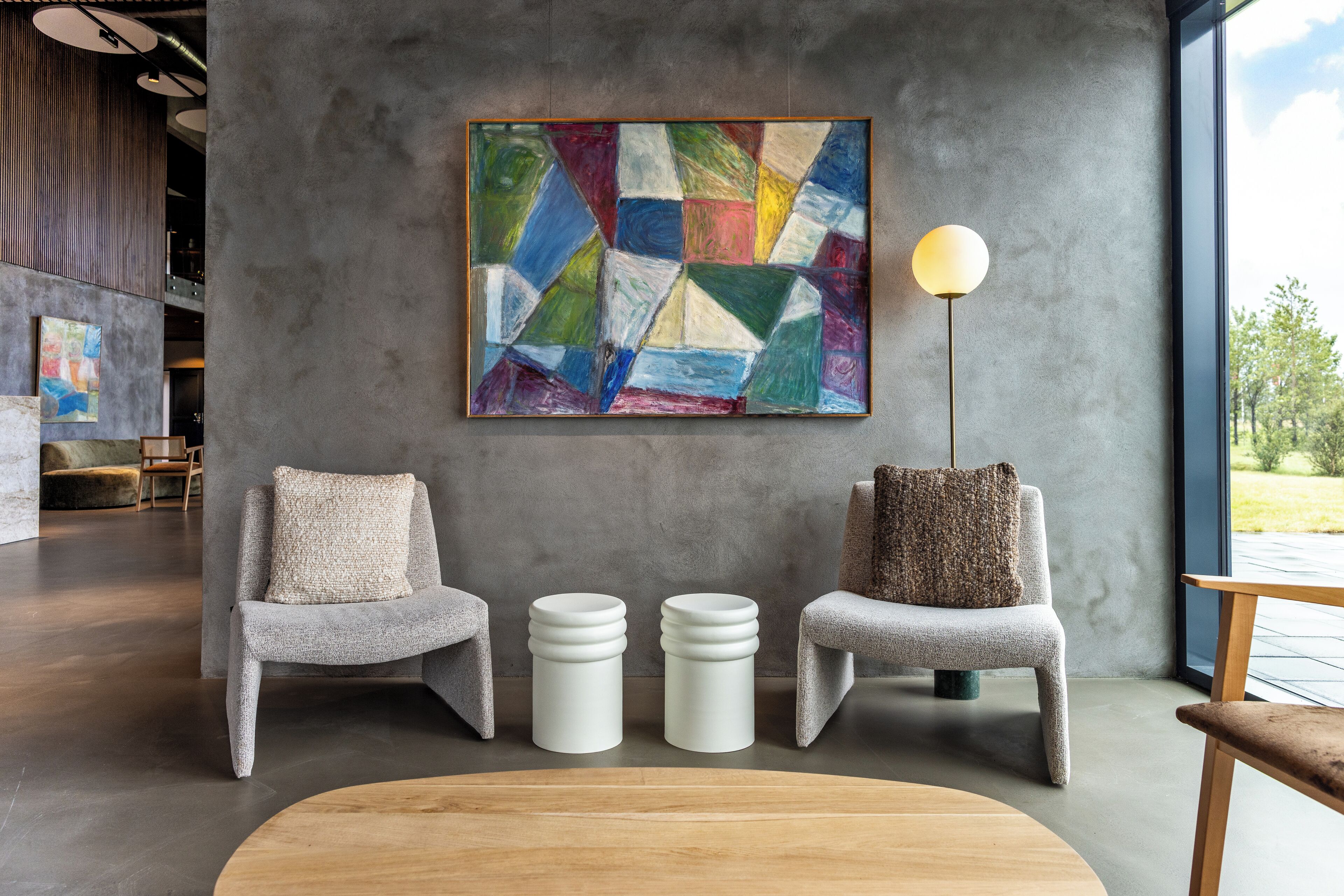 A modern interior with two grey armchairs, a wooden coffee table, and a colorful abstract painting on the wall.