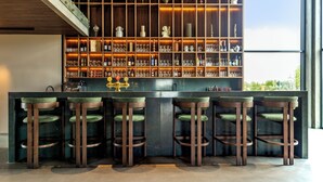A bar area with a dark counter, green cushioned stools, and shelves stocked with bottles and glasses. - Hotel Loa (Rangárþing eystra)