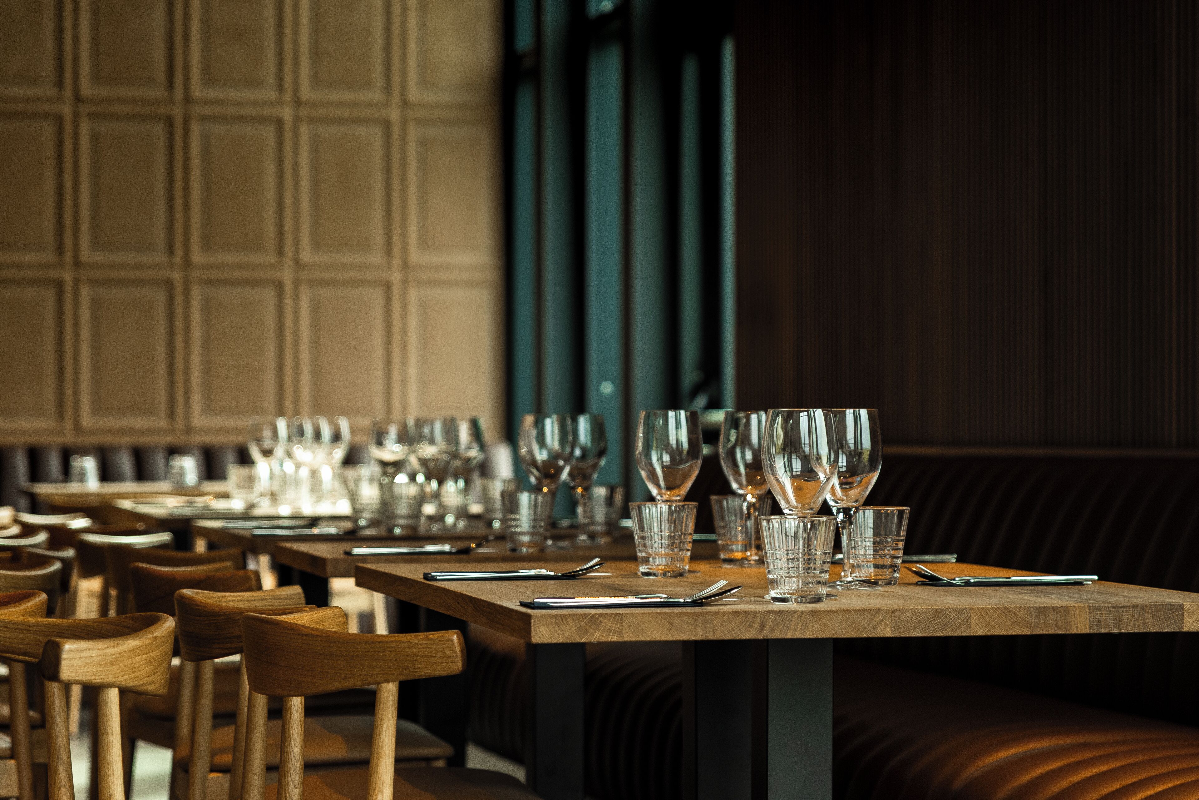Een restaurantinterieur met houten tafels, stoelen en een donkere houten wand met verticale panelen.