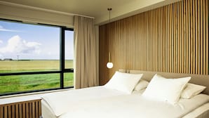 A modern hotel room with a large bed, a view of a green field, and a wooden slatted wall.