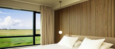 Une chambre d’hôtel moderne avec un grand lit, une vue sur un champ verdoyant et un mur avec des lambris en bois.