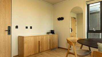 A modern room with a wooden cabinet, a dining table with chairs, and a large window.