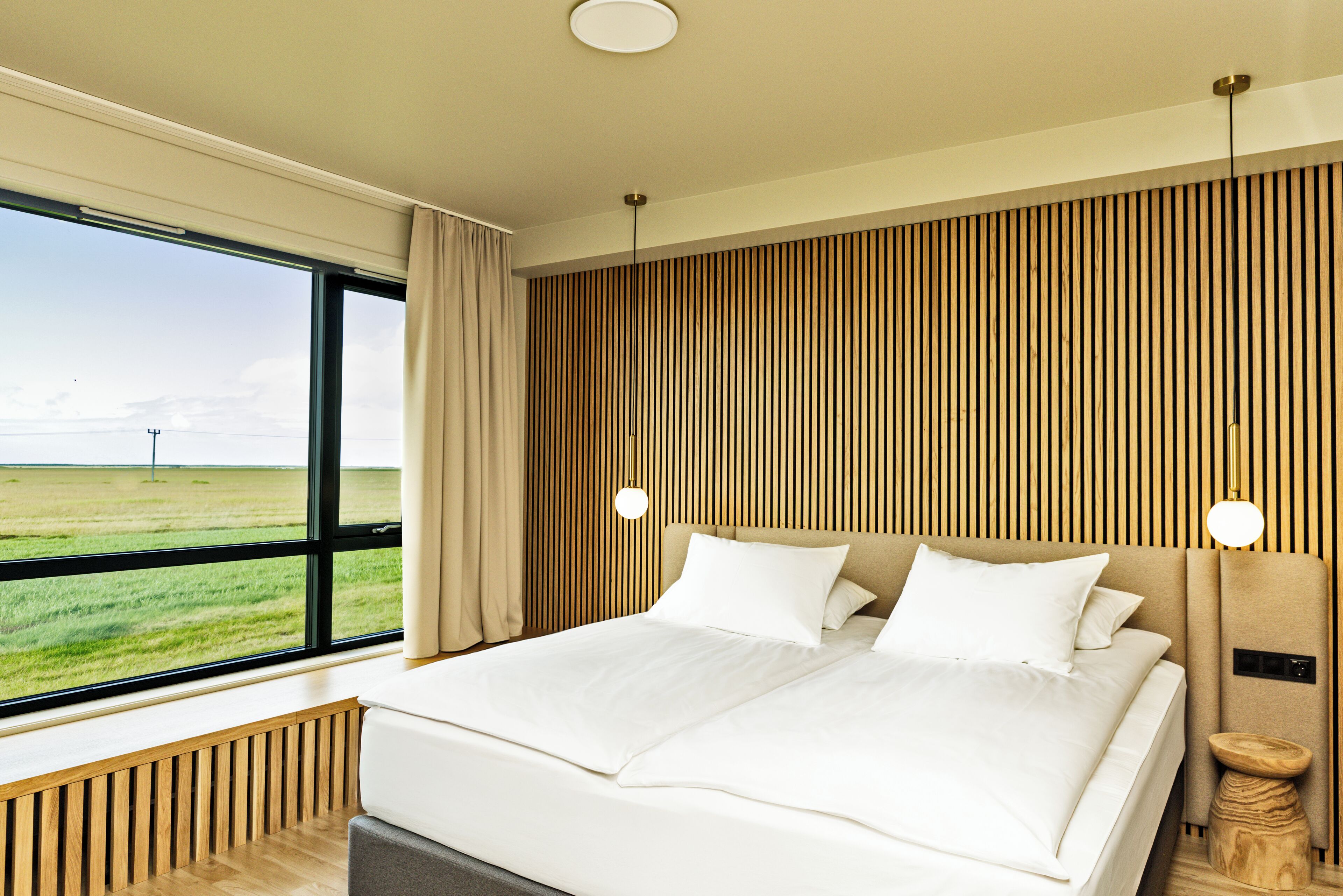 Una habitación de hotel moderna con una cama grande, vistas al campo y una pared de acento de madera.