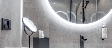 Een moderne badkamer met een ronde spiegel, een zwarte zeepdispenser en een handdouche.