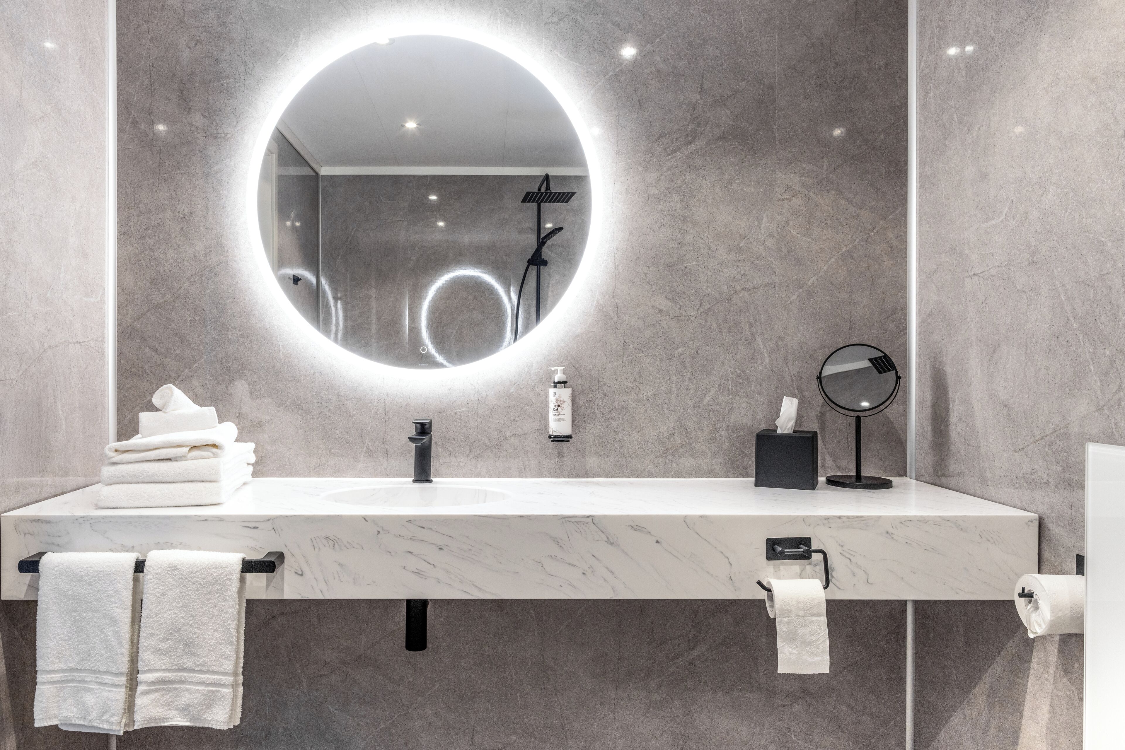 Un baño moderno con un lavamanos de mármol, un espejo redondo y un perchero para toallas.