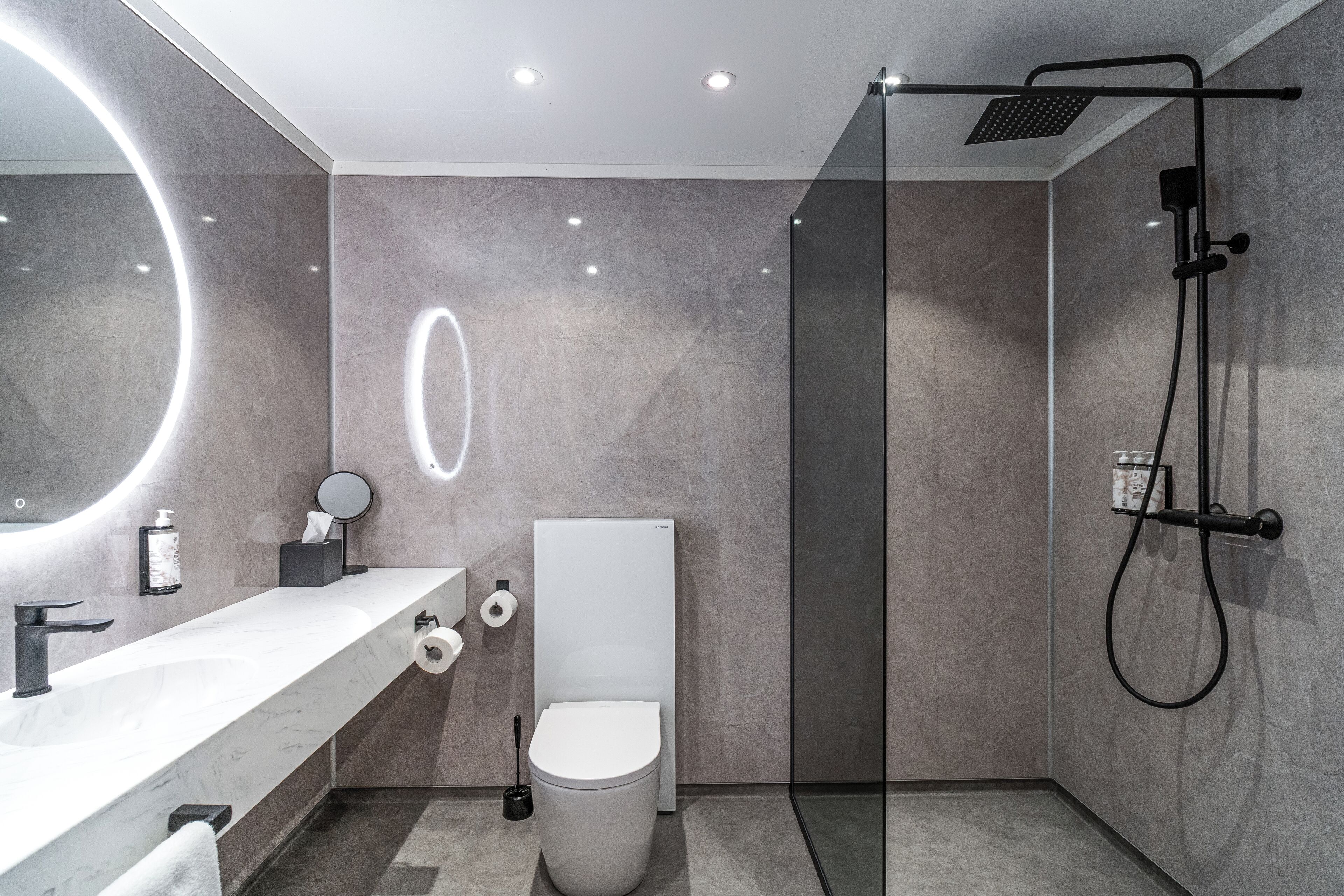A modern bathroom with a white vanity, a round mirror, a toilet, and a shower area.