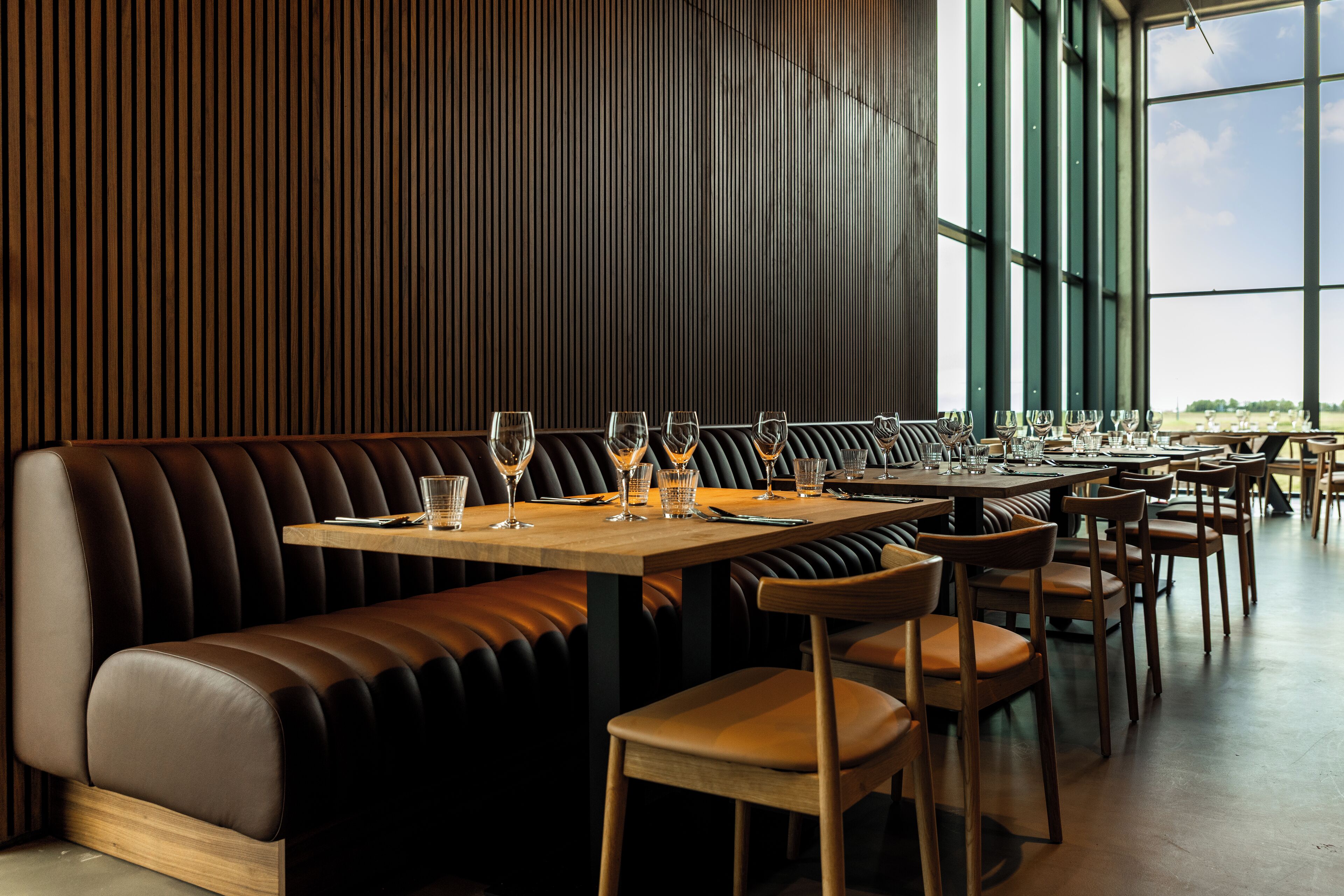 A restaurant with a long wooden bench seating area, multiple tables, and large windows offering a view.