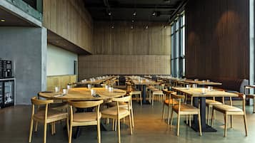 A spacious dining area with multiple tables and chairs, large windows, and a high ceiling.