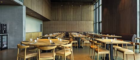 A spacious dining area with multiple tables and chairs, large windows, and a high ceiling.