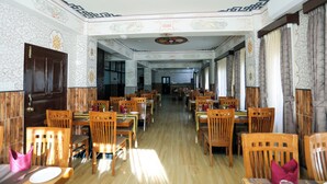 A spacious dining area with wooden tables and chairs, patterned walls, and a decorative ceiling. - Hotel Lhading (Thimphu)