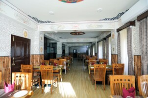 A spacious dining area with wooden tables and chairs, patterned walls, and a decorative ceiling.