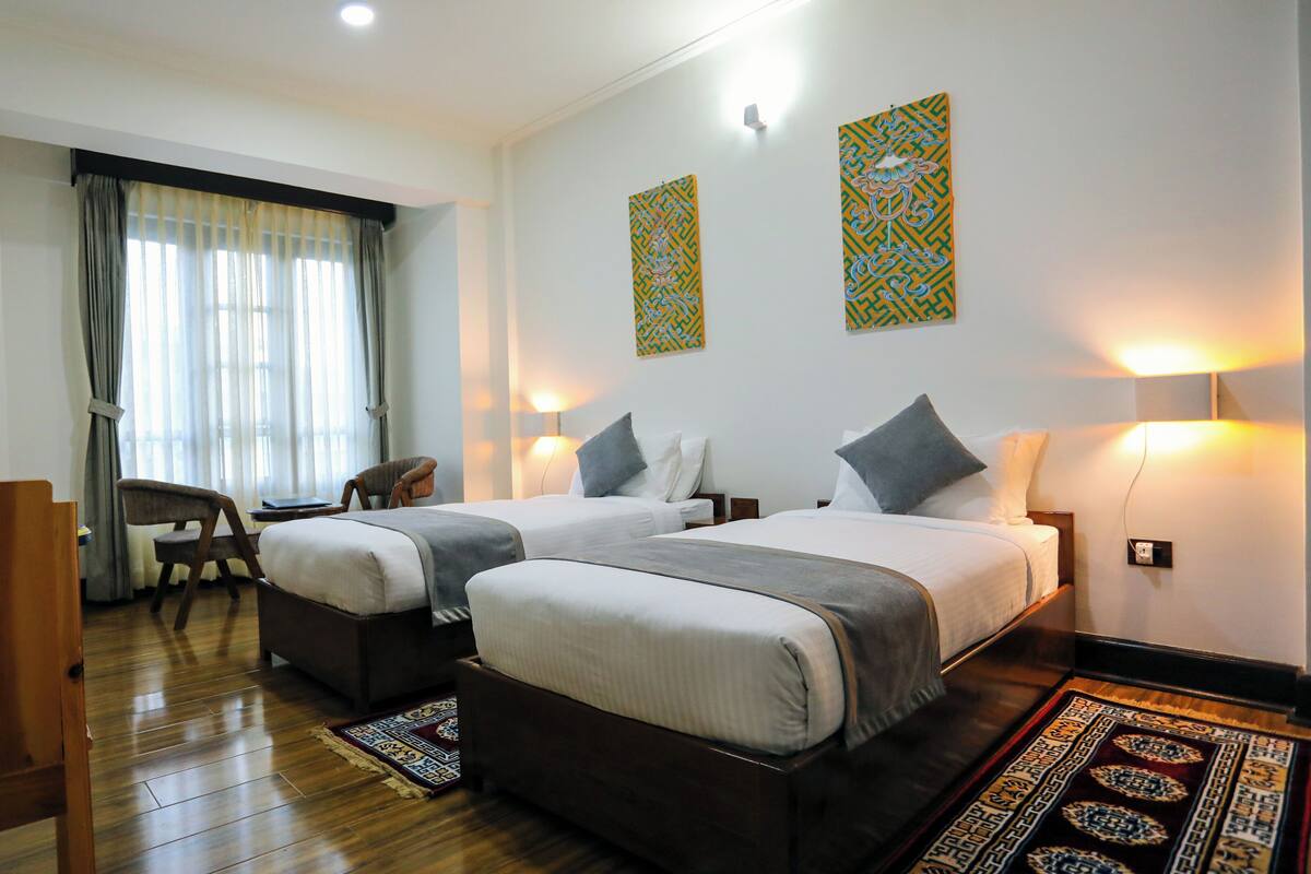 A hotel room with two beds, a desk, a chair, and a large window with curtains.