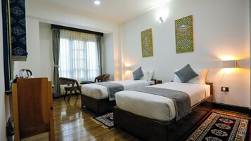 A hotel room with two beds, a desk, a chair, and a large window with curtains.
