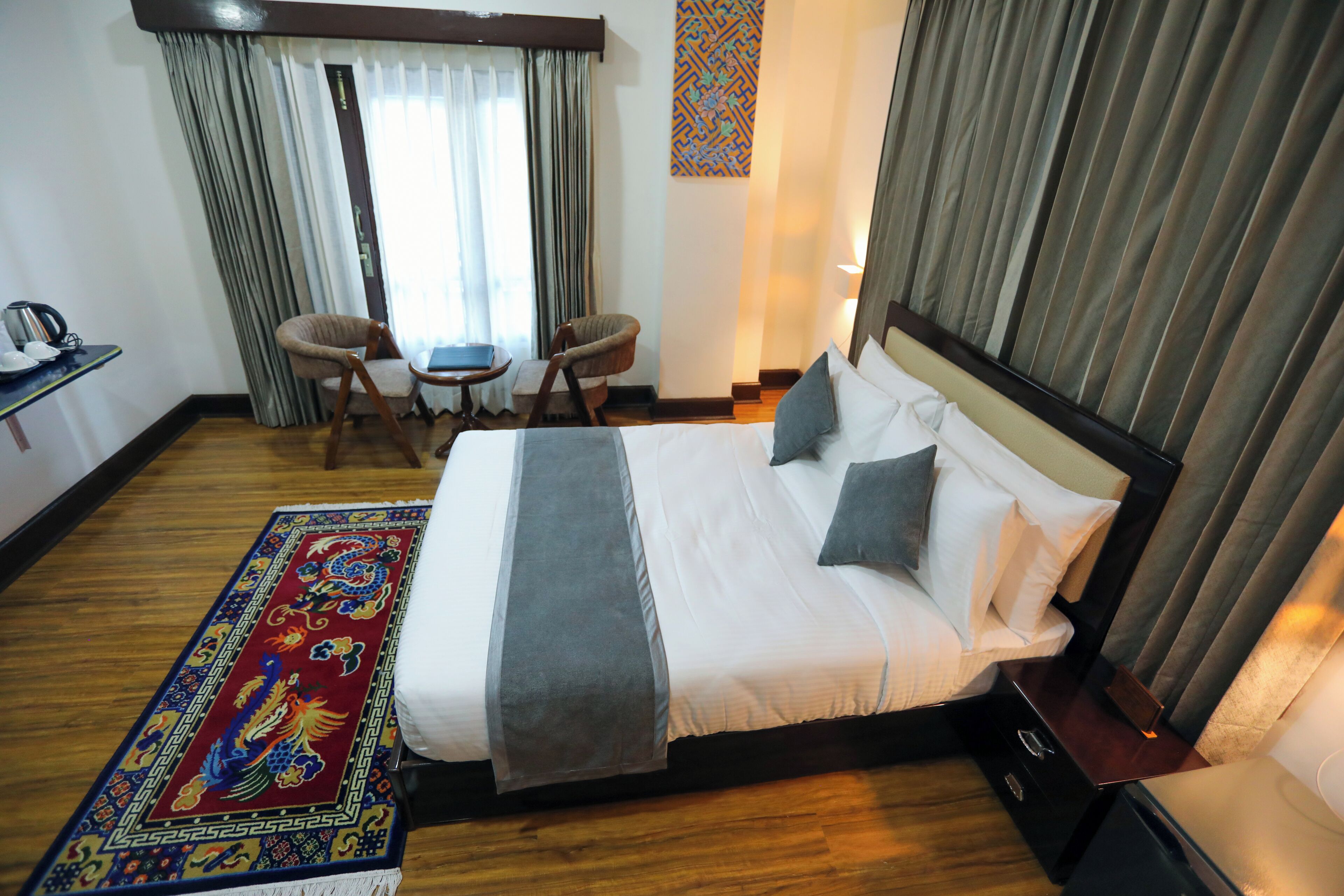 Een hotelkamer met een groot bed, een bureau met stoel, een klein tafeltje en een decoratief vloerkleed.