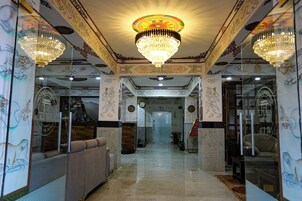 A hotel lobby with ornate ceiling decorations, chandeliers, and traditional wall art.
