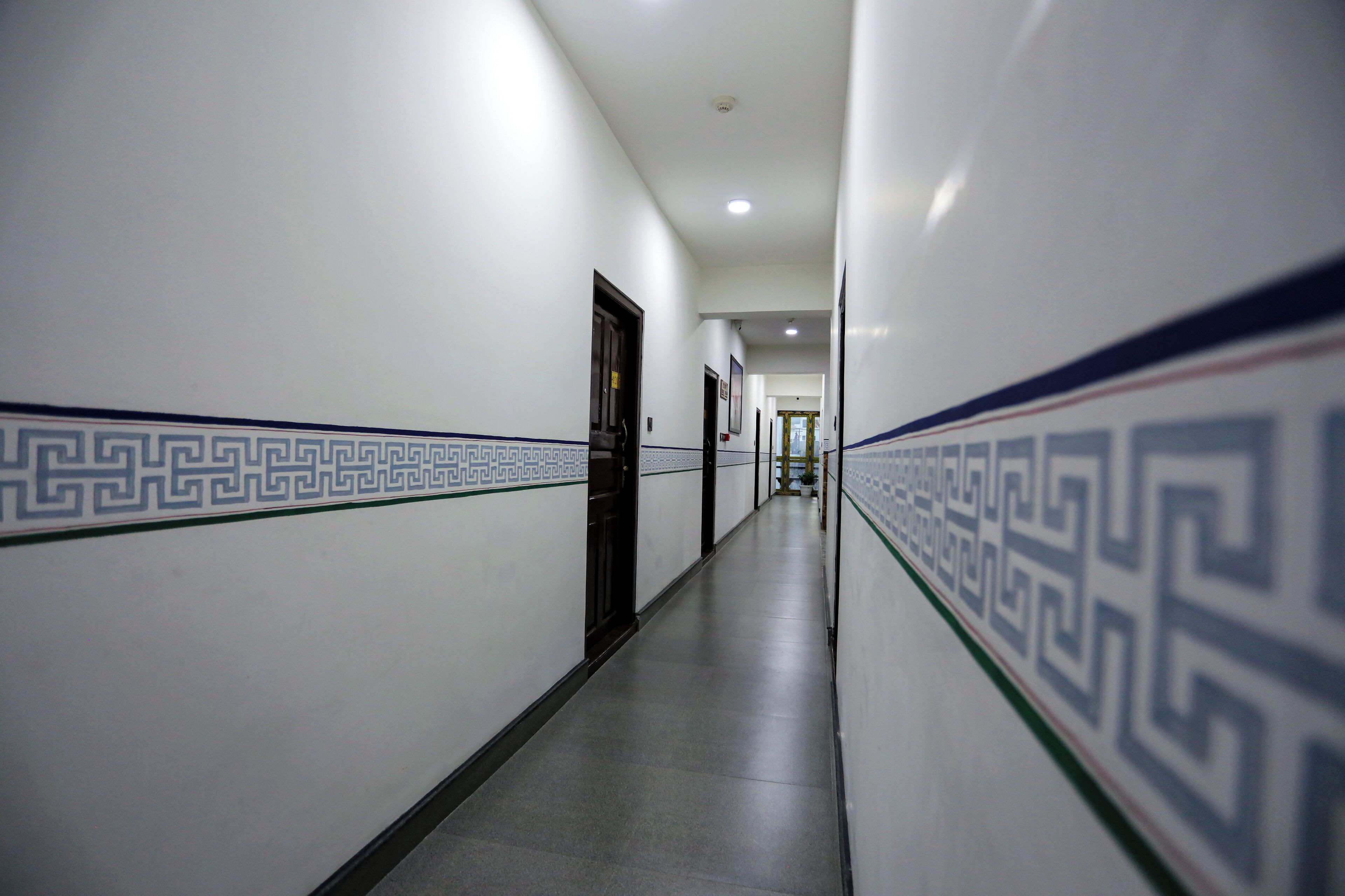 A long, narrow hallway with patterned walls and a tiled floor, leading to a door at the end.