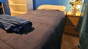 A neatly made bed with a blue blanket, a bedside table with a potted plant, and a blue wall. - Guesthouse - Metro M1 Sesto Rondò (Sesto San Giovanni)
