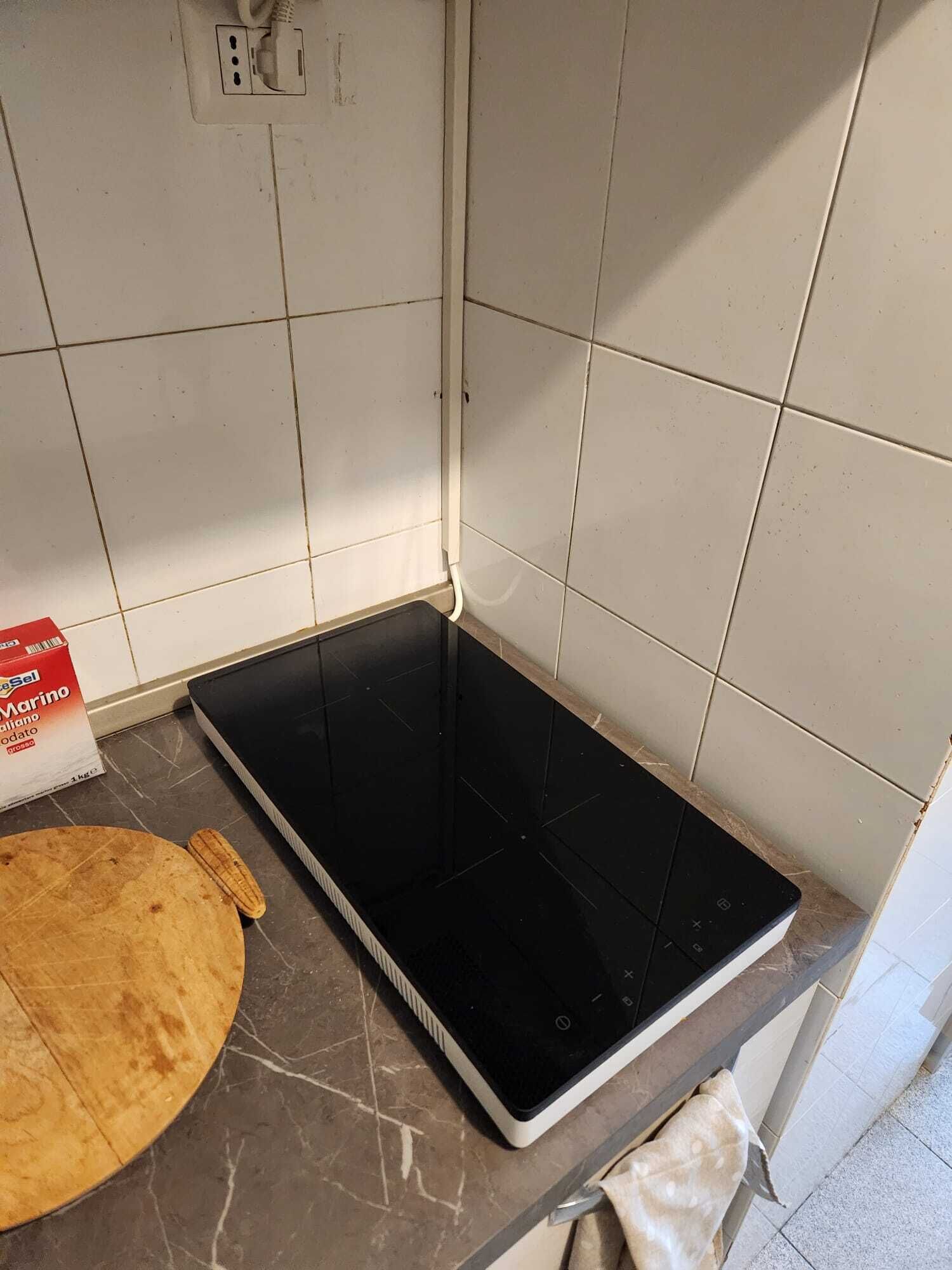 Eine Küche mit weißen Fliesenwänden, einer schwarzen Induktionskochplatte, einem Holzschneidebrett und einer Packung 'Marino'-Pasta.
