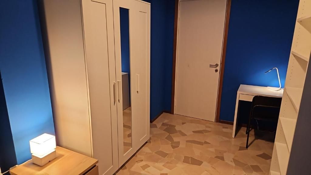 A room with a wardrobe, a desk, and a chair.