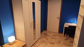 A room with a wardrobe, a desk, and a chair.