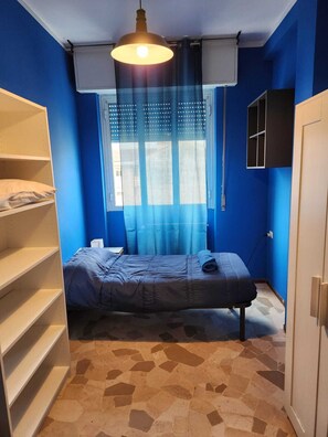 Ein Zimmer mit einem Bett, einem Kleiderschrank und einem Fenster mit Vorhängen.