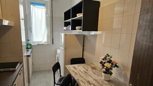 A compact kitchen with a wooden table, chairs, a window with curtains, and a black shelf above the counter. - Guesthouse - Metro M1 Sesto Rondò (Sesto San Giovanni)