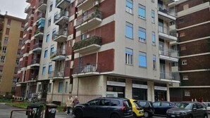 A multi-story residential building with balconies, a parking area, and a street in front. - Guesthouse - Metro M1 Sesto Rondò (Sesto San Giovanni)