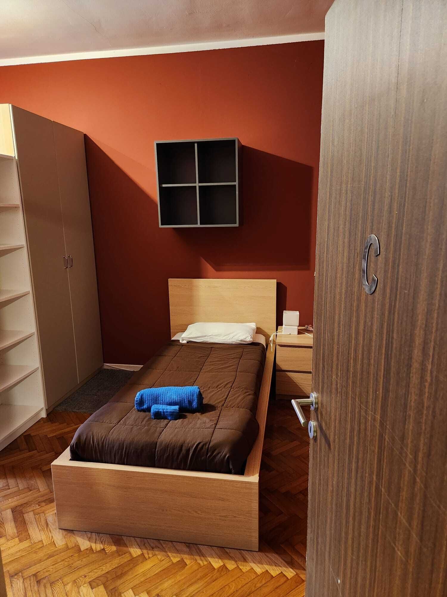 Ein Schlafzimmer mit einem hölzernen Bett, einem Kleiderschrank, einem kleinen Nachttisch und einem an der Wand befestigten Regal.