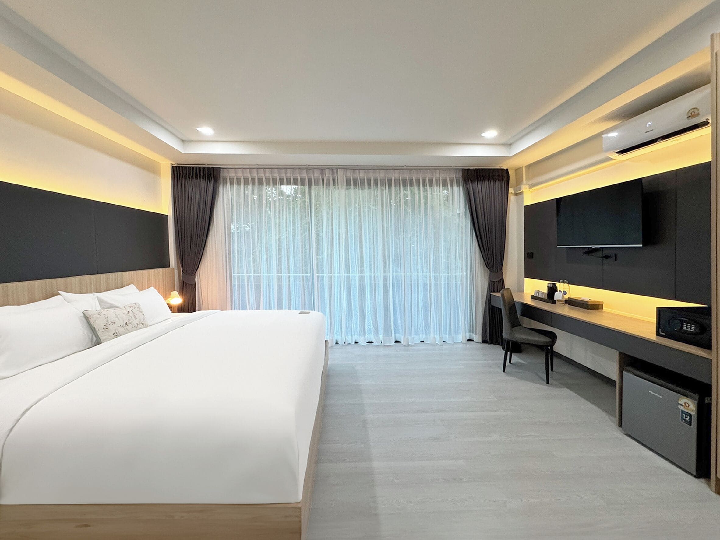 Una habitación de hotel moderna con una cama grande, un escritorio con silla, televisión y minibar.