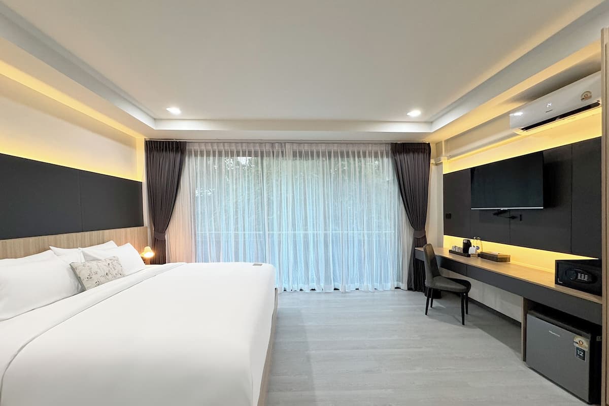 Una habitación de hotel moderna con una cama grande, un escritorio con silla, televisión y minibar.
