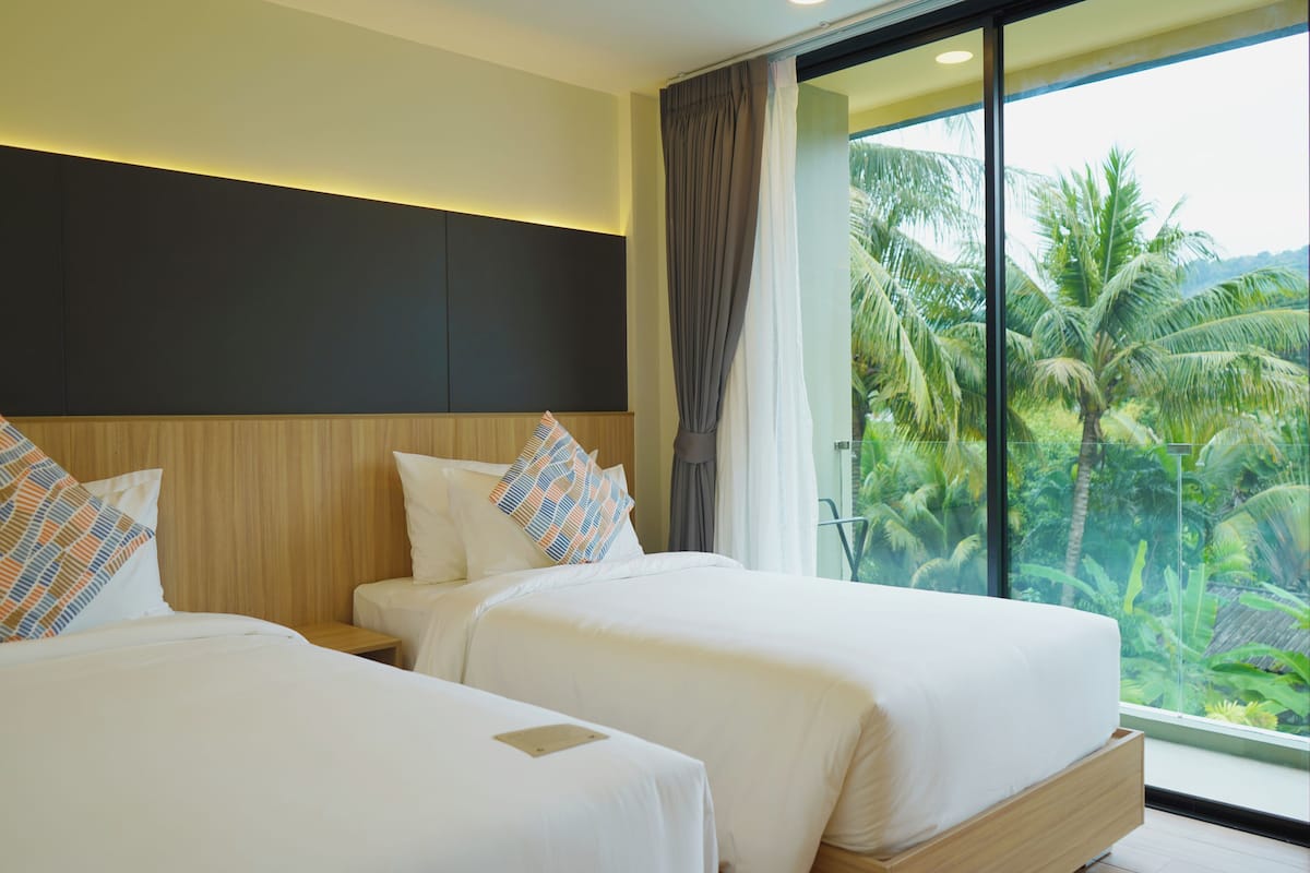 Habitación de hotel con dos camas, un ventanal con vistas a palmeras y un diseño moderno.