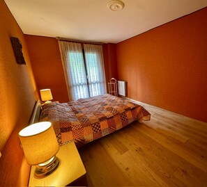 Una camera da letto con un letto, un comodino con lampada, una finestra con tende e un termosifone.