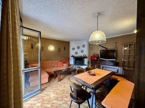 Een woonkamer met een bank, een eettafel met stoelen, een televisie en een open haard.