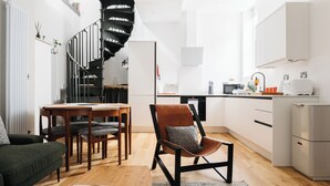 Un apartamento moderno con una escalera de caracol, un comedor, una sala de estar con sofá y mesa de centro, y una cocina con armarios y electrodomésticos blancos.