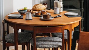 Un comedor con una mesa de madera dispuesta para el desayuno, incluyendo pan, bollería y una cafetera.