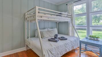 A bunk bed with a ladder, a bedside table with a plant, and a window with a view of greenery.