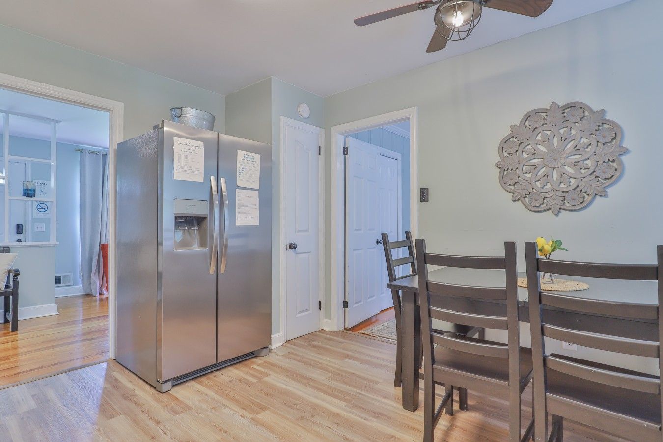 A kitchen with a stainless steel refrigerator, a dining table with chairs, and a decorative wall piece.