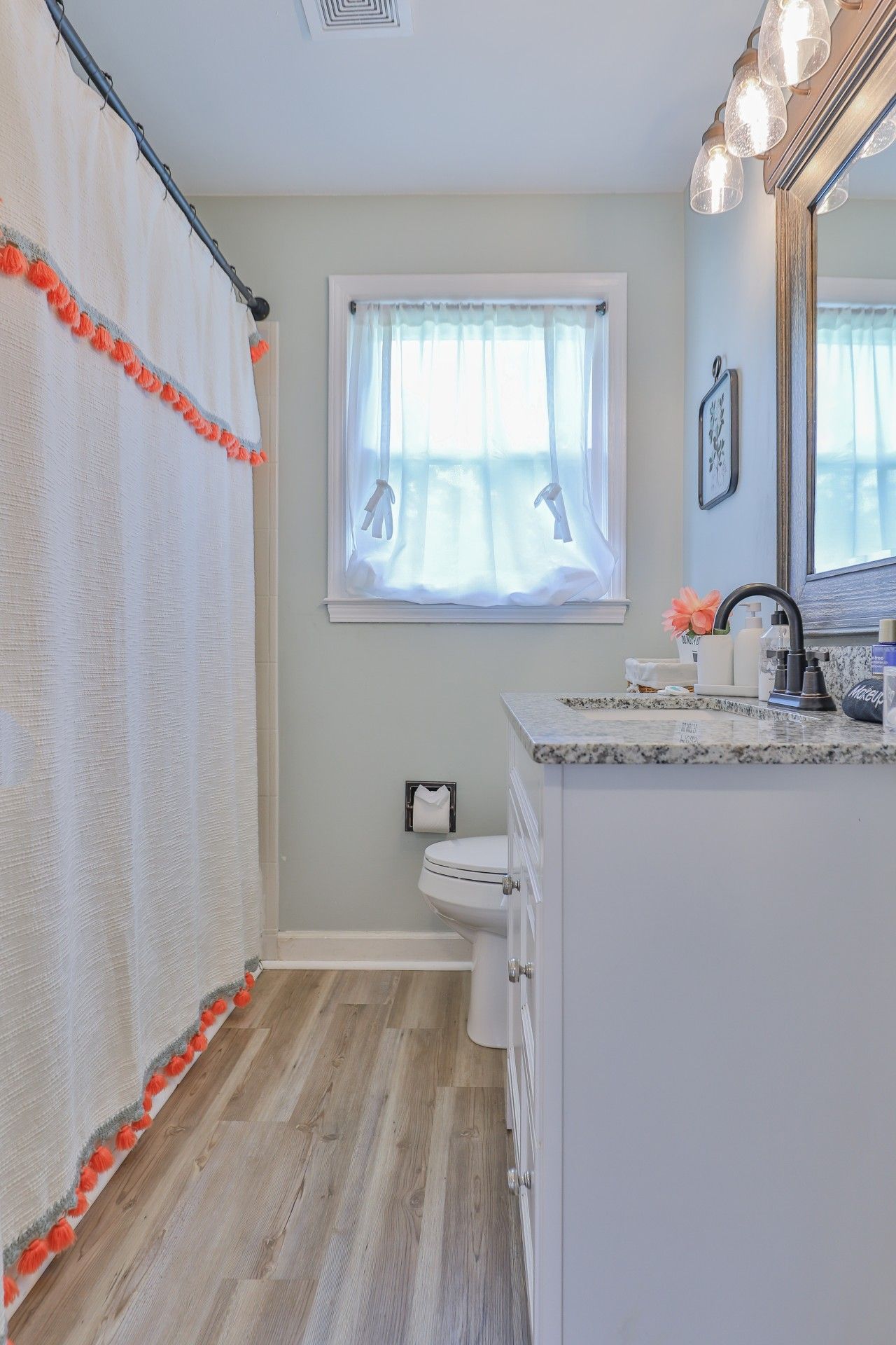 A bathroom with a toilet, a sink with a mirror, and a window with a curtain.