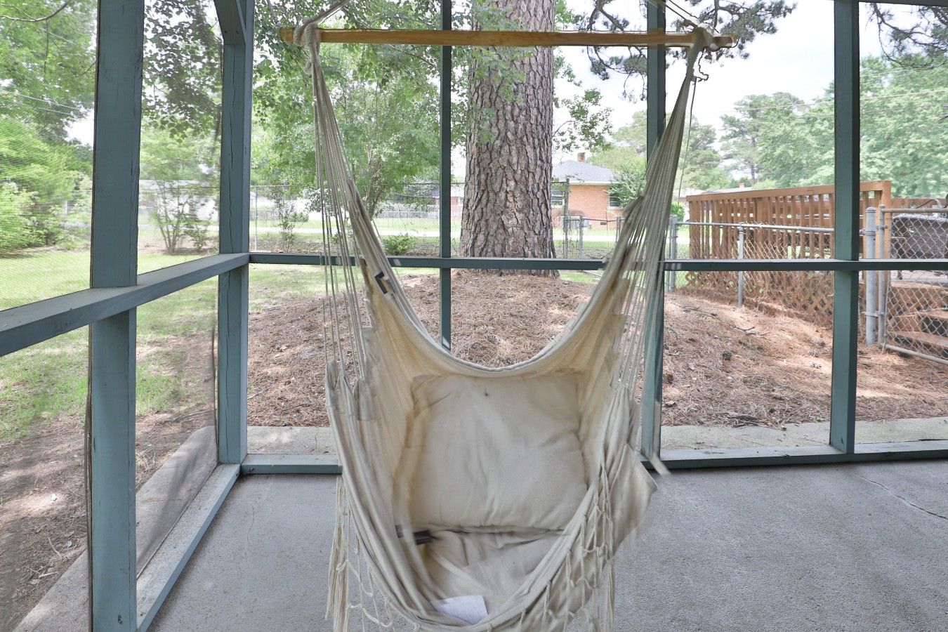 A hammock suspended from a metal frame, with a view of a fenced outdoor area and trees in the background.