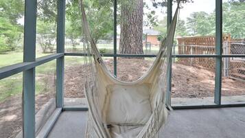 A hammock suspended from a metal frame, with a view of a fenced outdoor area and trees in the background.