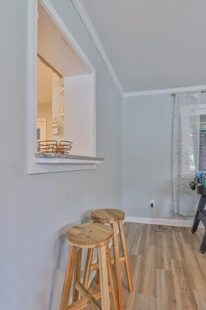 Una habitación con un ventanal grande, taburetes de madera, una pared blanca y suelo de madera.