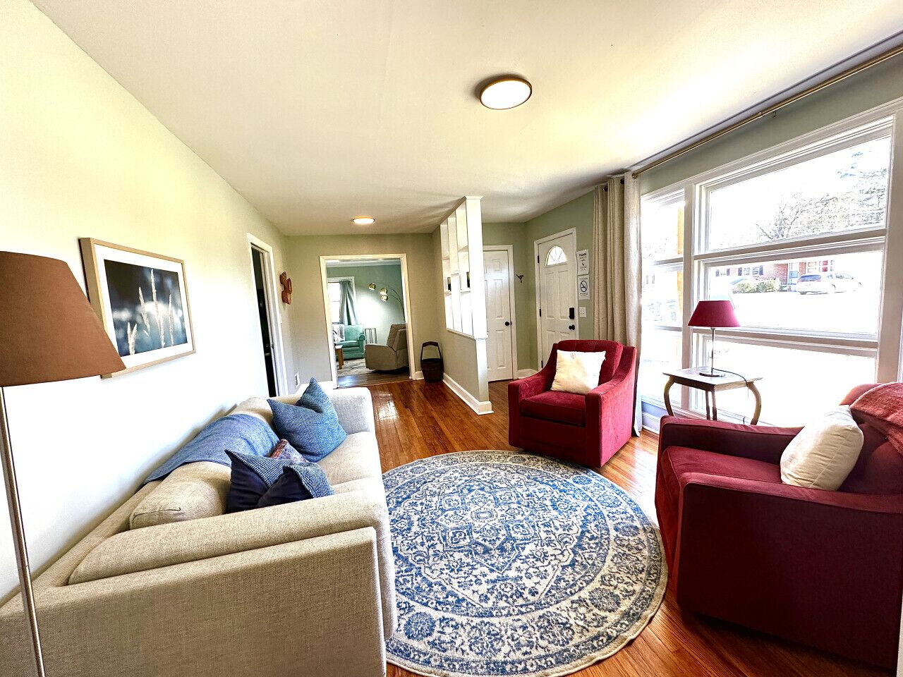 A modern living room with a beige sofa, red armchairs, and a blue patterned rug.