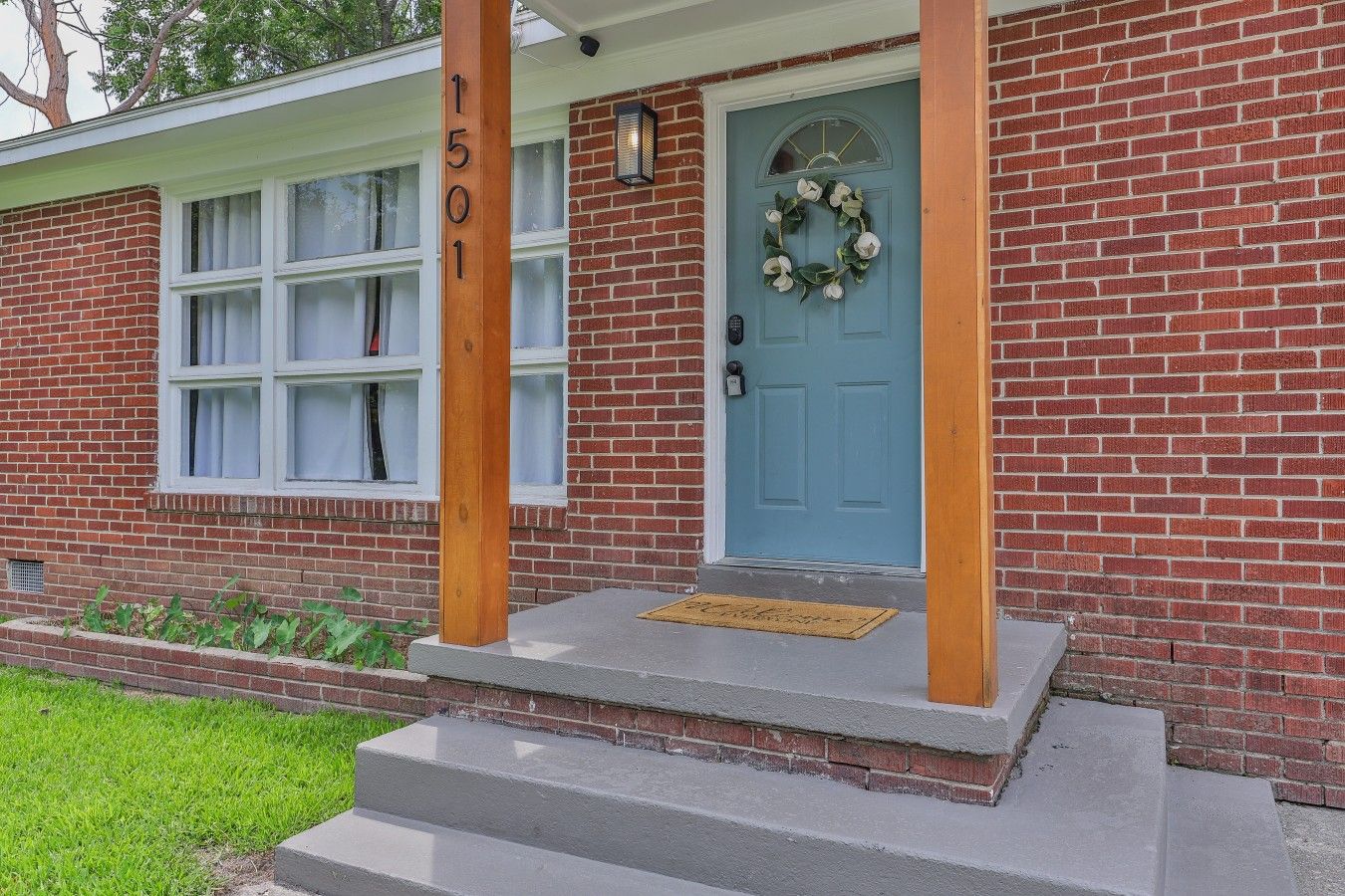 A brick house with a blue door, a number '1501' on a wooden post, and a wreath on the door.