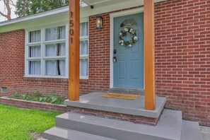 A brick house with a blue door, a number '1501' on a wooden post, and a wreath on the door.