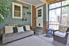 Ein gemütlicher Wohnbereich mit einer Couch, einem Sessel und einem Fenster mit Blick auf ein Backsteingebäude.