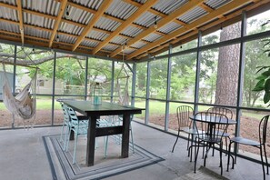 A covered patio with a table and chairs, a hammock, and a view of the outdoors.
