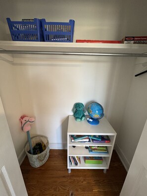 Un pequeño espacio de estudio con un estante blanco que contiene libros, un globo terráqueo, una cesta azul y una figura de caballo rosa.