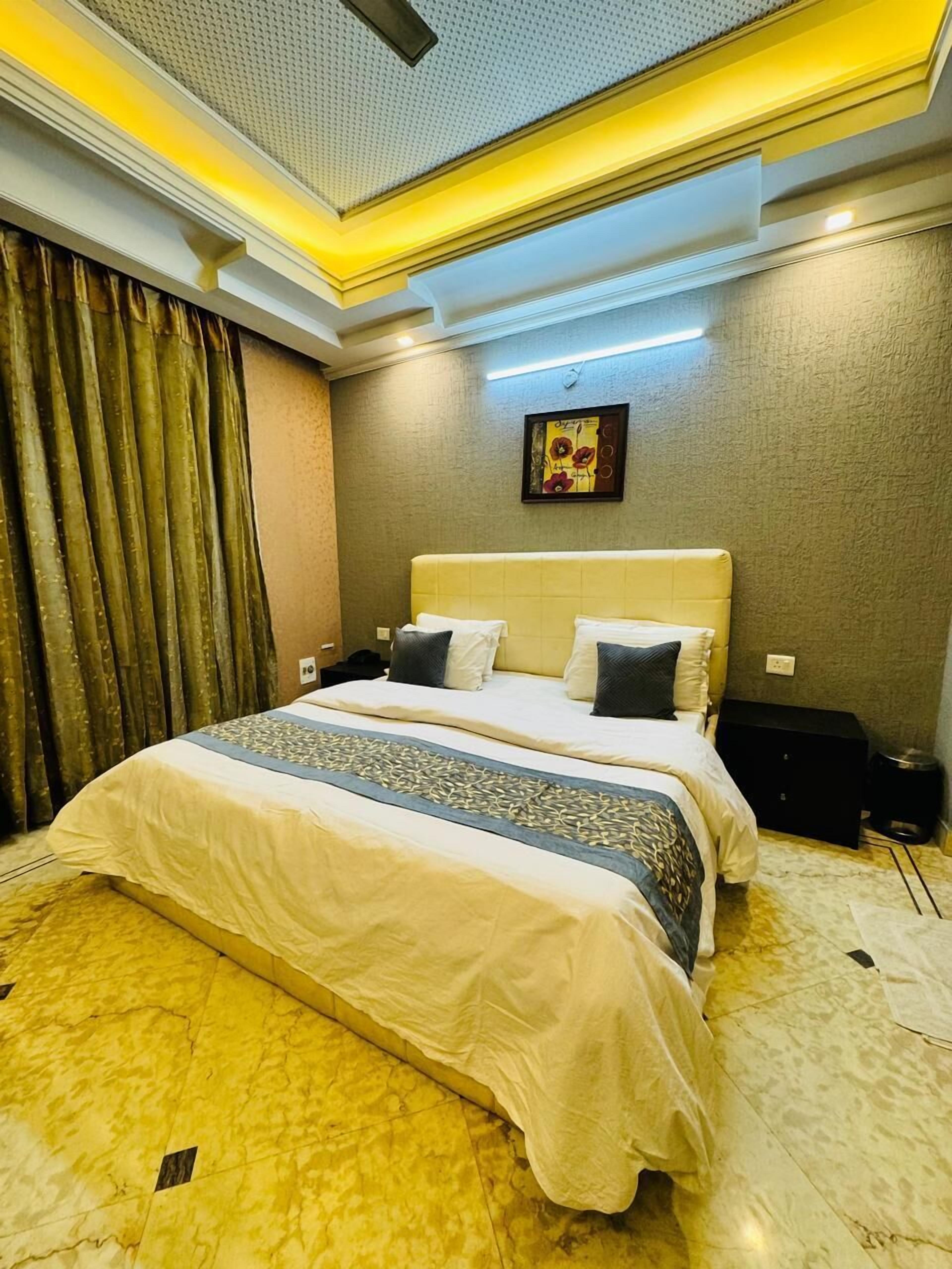 A hotel room with a large bed, a headboard, a nightstand, a wall-mounted clock, and a framed artwork.