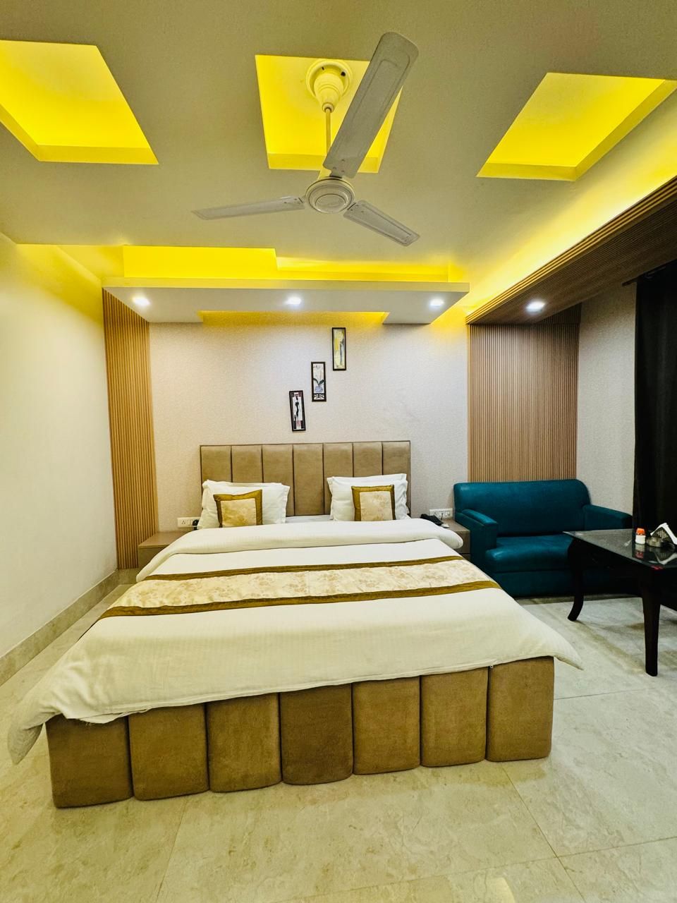 A modern bedroom with a large bed, a ceiling fan, recessed lighting, and a blue sofa.