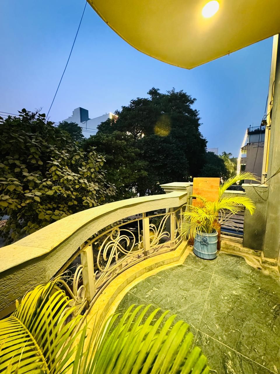 Un balcon doté d’une balustrade incurvée, d’un pot de fleurs et offrant une vue sur les arbres et les bâtiments.